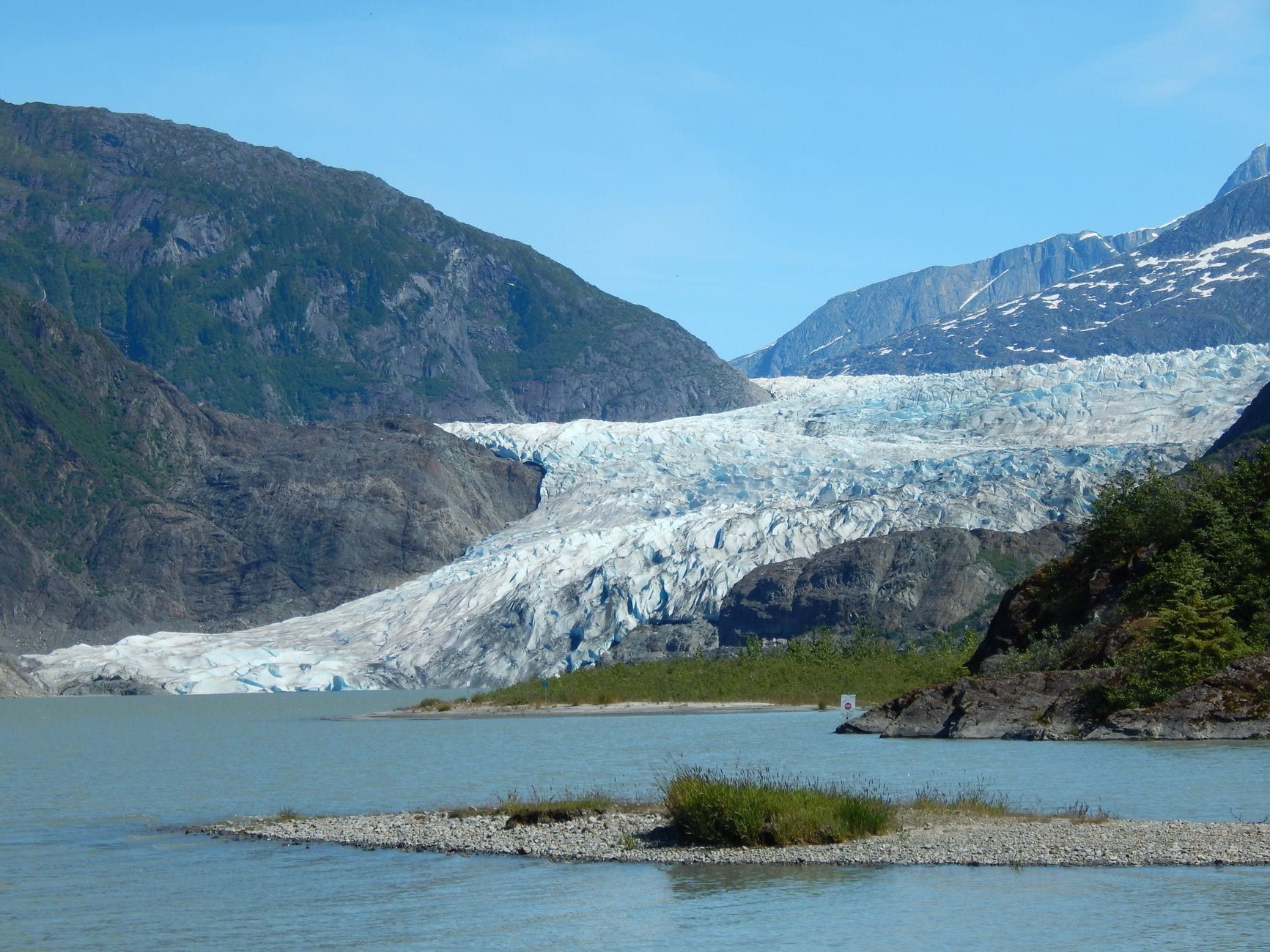 Weitwinkelblick auf den Mendenhall-Gletscher, der zwischen rauen Bergen unter einem klaren blauen Himmel zum Mendenhall Lake hinabfließt.